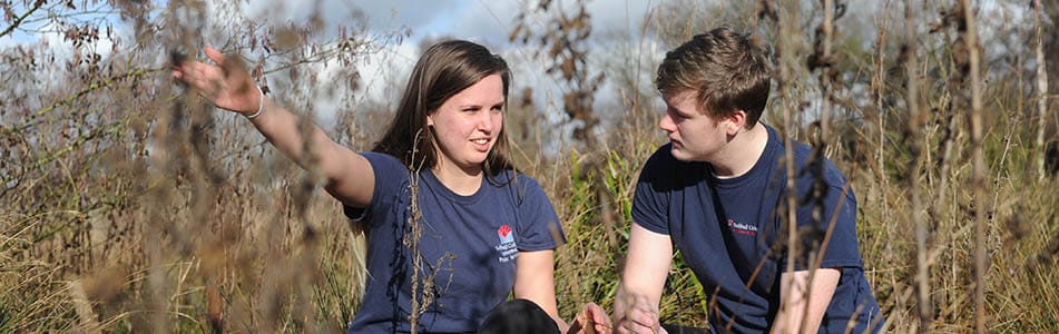 Two students in a field surrounded by weeds